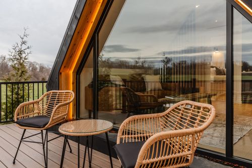 Deck seating nook with a round table and wicker chairs beside the A-frame cabin's glass wall