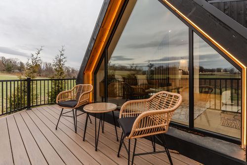 Deck seating with wicker chairs and round table beneath the A-frame cabin's glowing gable at dusk