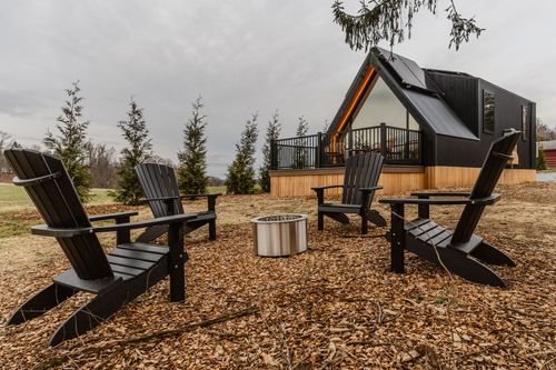 Four black Adirondack chairs around a fire pit with the A-frame cabin glowing behind them