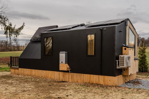 Black modern cabin exterior with rooftop solar panels, HVAC units and cedar wood skirting