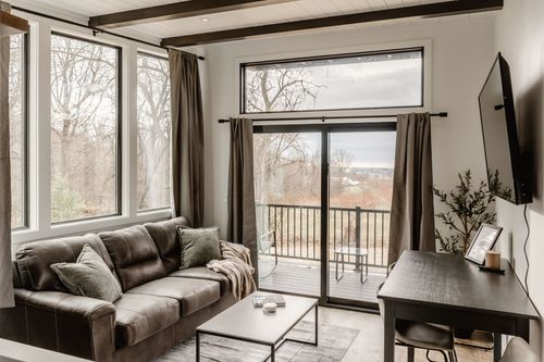 Living room with a leather sofa, wood beam ceiling and glass door opening onto a balcony over the orchard