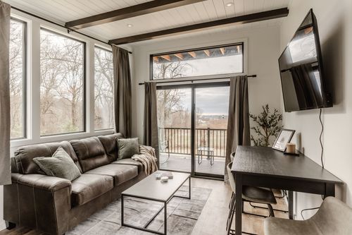 Living room with a leather sofa, wall-mounted TV and wood beam ceiling beside a glass balcony door