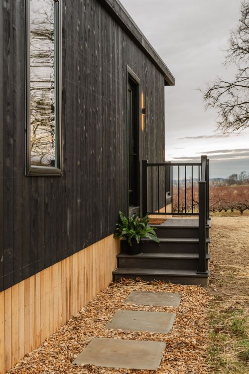 Close view of a black cabin's covered deck and stone stepping-stone path overlooking open land