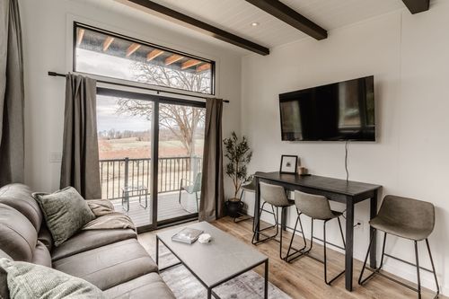 Living room with exposed wood beam ceiling, wall-mounted TV, gray sectional and sliding glass door