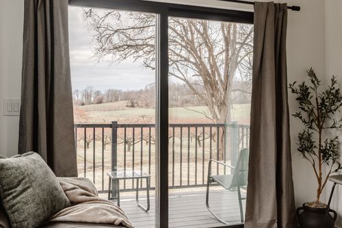 Sliding glass door framing rolling farmland, sheer curtains and a small balcony seating area