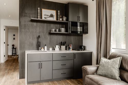 Dark ribbed-wood kitchenette with black cabinets, open shelving and a matte black faucet