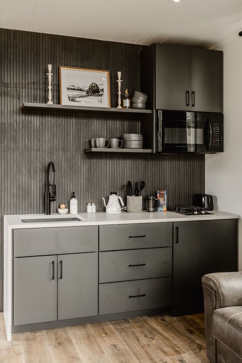 Kitchenette shelf styled with framed landscape art, candlesticks, mugs and a black microwave