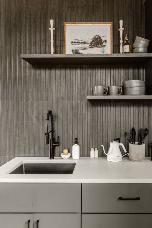 Close view of a dark kitchenette wall with styled shelves, black faucet and gas cooktop