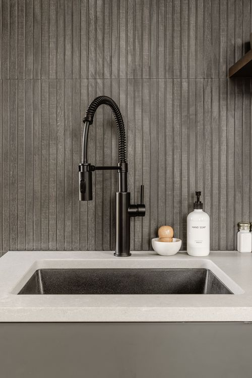 Matte black pull-down faucet over a concrete-look sink against a ribbed wood backsplash
