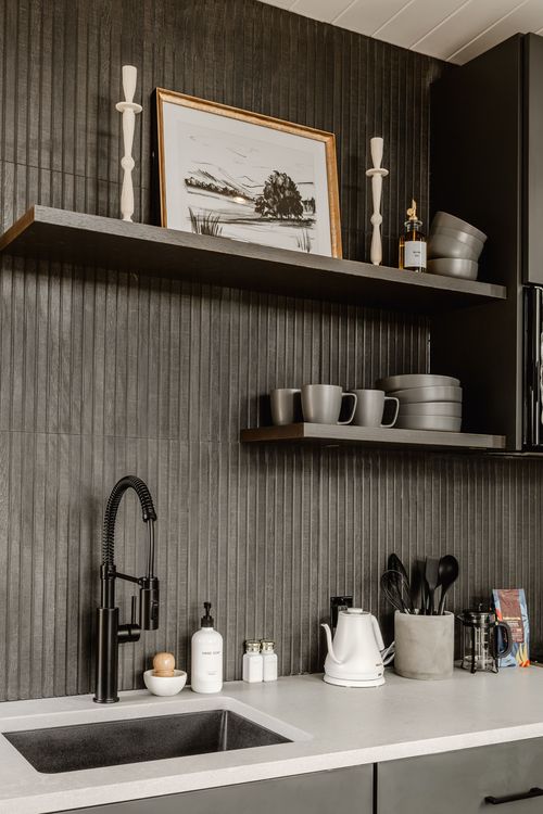 Kitchenette corner with open wood shelving, black faucet, kettle and dark cabinetry