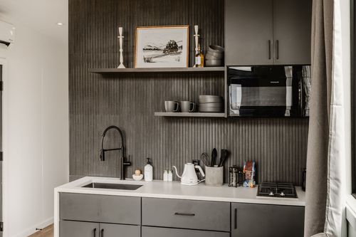 Wide kitchenette view with ribbed dark wall, black fixtures, cooktop and linen curtain edge