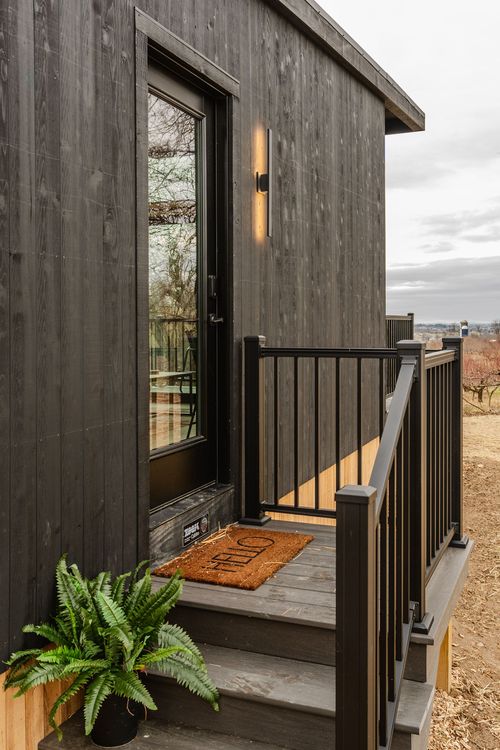 Cabin entry with black door, sconce light, welcome mat and potted fern on the deck