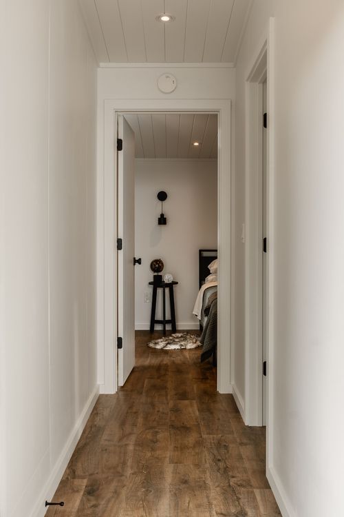 Hallway view down a wood-floored corridor into a bedroom with a black side table and globe