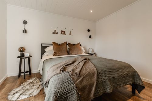 Cozy bedroom with wood-paneled ceiling, wall sconces, layered bedding and a round side table