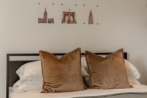Brown velvet throw pillows on a bed beneath minimalist New York skyline wall art