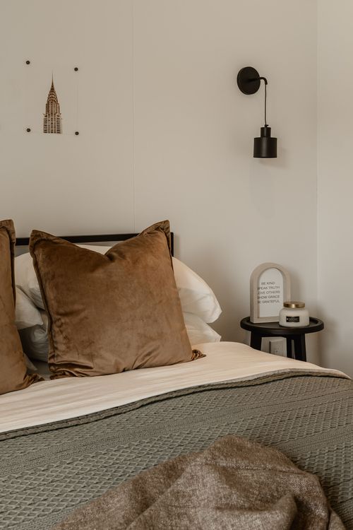 Close-up of a velvet throw pillow, black pendant sconce and a candle on a bedside table