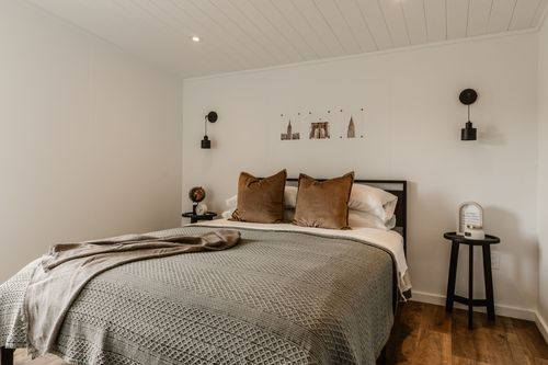 Bedroom with sloped shiplap ceiling, wall sconces, sage knit bedspread and wood flooring