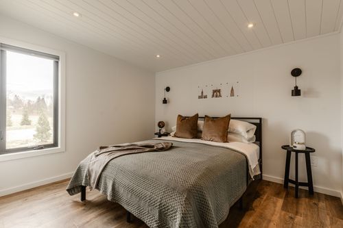 Bedroom with a large window overlooking farmland, sage bedspread and warm wood floors