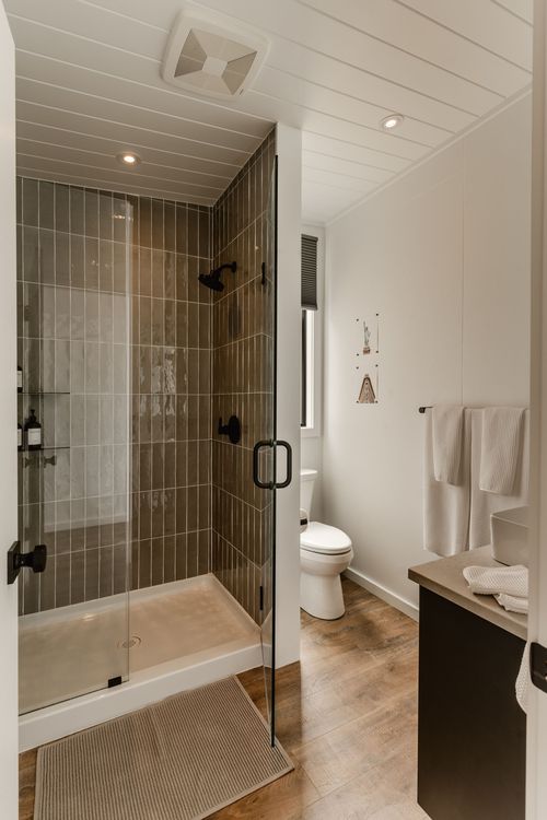 Bathroom with a tiled walk-in glass shower, black fixtures, toilet and wood-look flooring