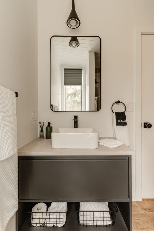 Close view of an arched black mirror, vessel sink and hanging makeup towel ring
