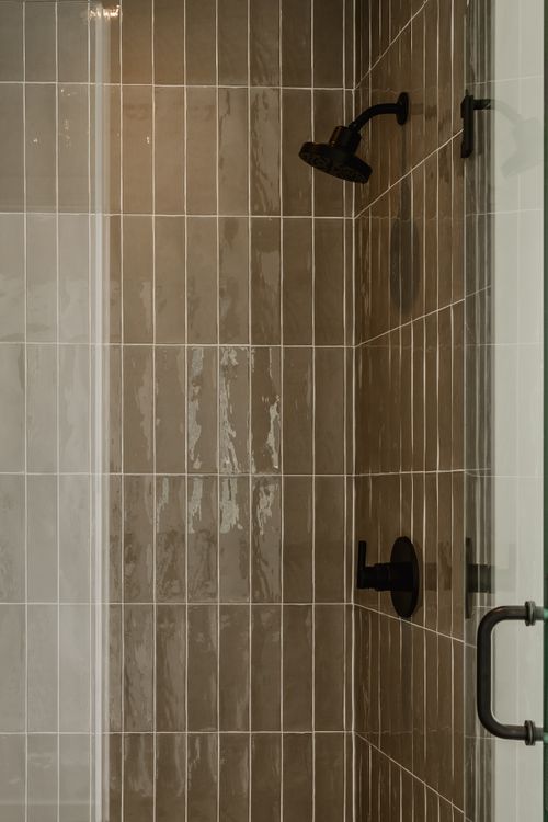 Close-up of a tiled shower with black fixtures and a frameless glass door