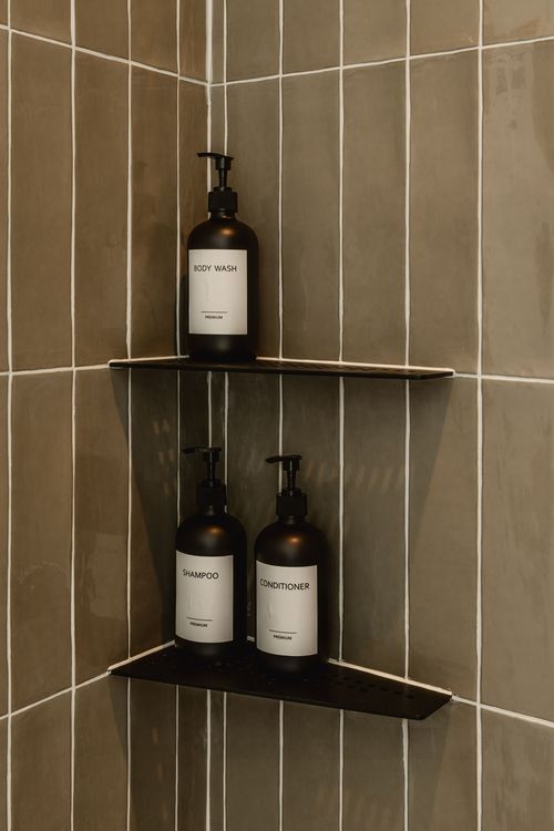 Shower corner shelves holding amber glass bottles of body wash, shampoo and conditioner