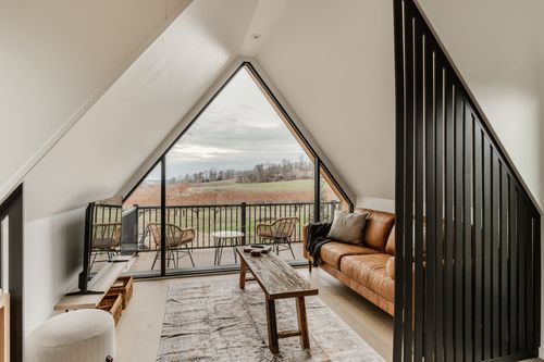 A-frame loft living space with a peaked window wall, tan leather sofa and balcony view