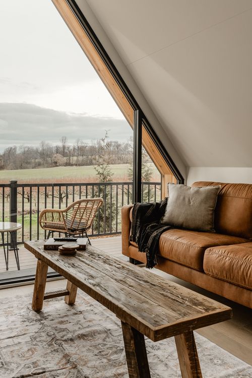 Peaked A-frame window seating nook with leather sofa, wood bench and layered area rug