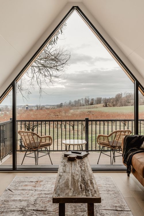 Peaked window framing rolling farmland and orchard rows above rattan balcony chairs