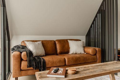 Tan leather sofa with cream throw pillows against a black slat wood room divider