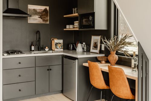 Compact kitchenette with charcoal cabinets, range hood and orange leather dining chairs