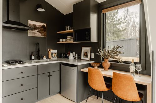 Dark kitchenette cooktop and cabinets beside an orange leather chair dining nook
