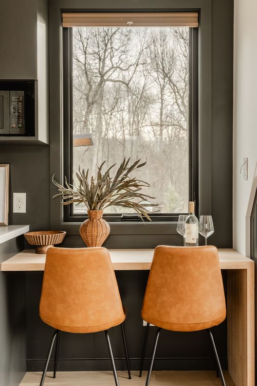 Window dining nook with orange leather chairs and a woven vase of dried grasses