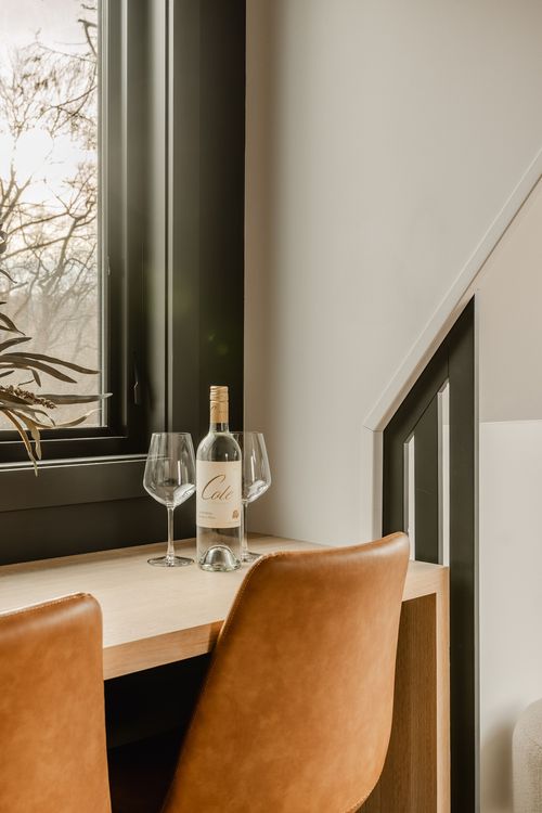 Wood counter styled with a wine bottle and glasses beside a dark window frame