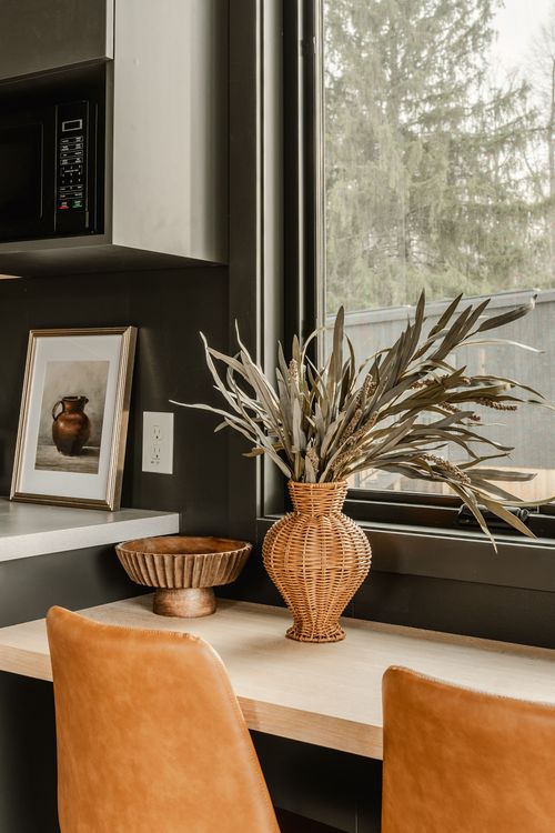 Dining nook counter with framed art, a wicker vase of dried grass and leather chairs