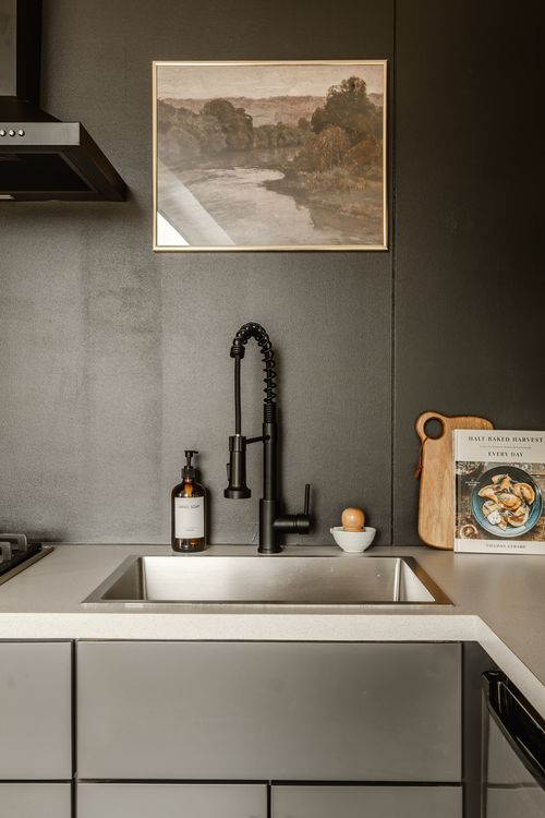 Kitchen sink styled with framed landscape art, soap and a wood cutting board