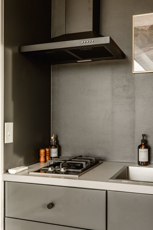 Range hood over a gas cooktop with a pepper mill and framed art in a dark kitchenette