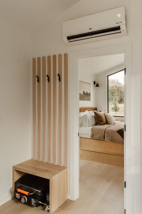 Entryway with wood slat coat hooks, a wall heater and a view into a cozy bedroom
