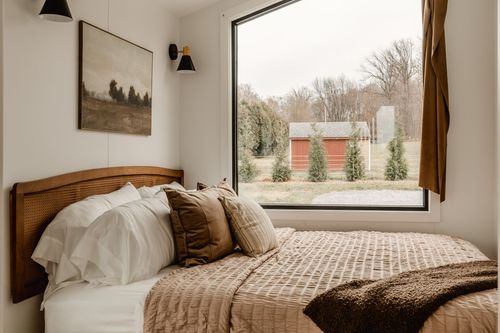 Close view of a cane headboard and brown pillows with a red barn visible through the window