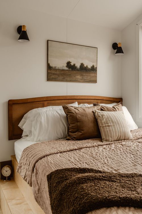 Cane headboard bed with brown velvet pillows, an alarm clock and landscape art above