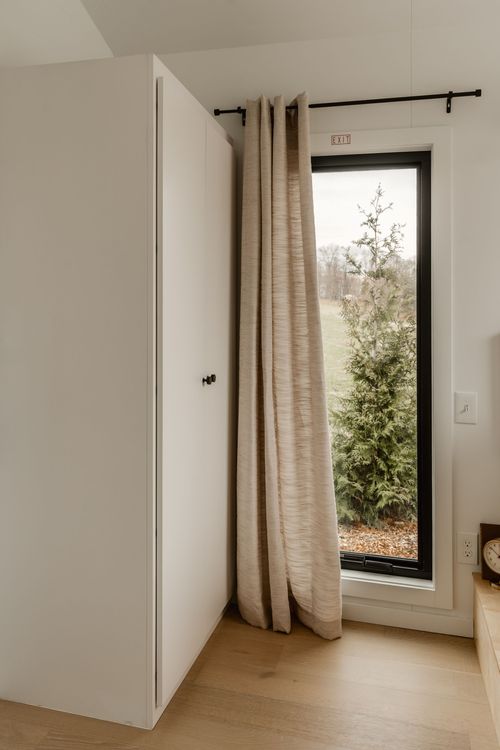 Tall curtained window beside a white wardrobe door in a bright bedroom nook