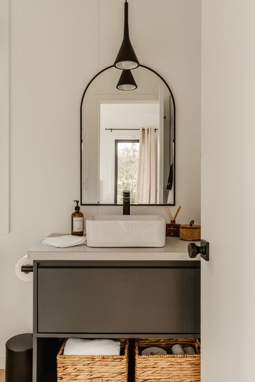 Bathroom vanity with an arched pendant light, black mirror, vessel sink and woven baskets