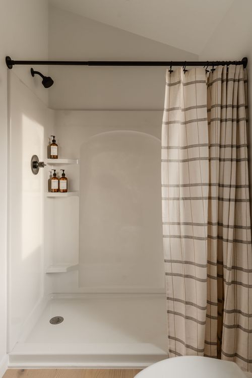 Shower with a striped curtain, arched tiled niche and matte black fixtures