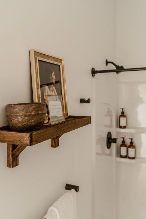 Wall shelf styled with a framed portrait and small bowl beside a glass shower