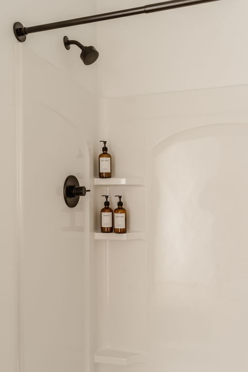Shower corner with amber soap dispensers on a white built-in shelf and black fixtures