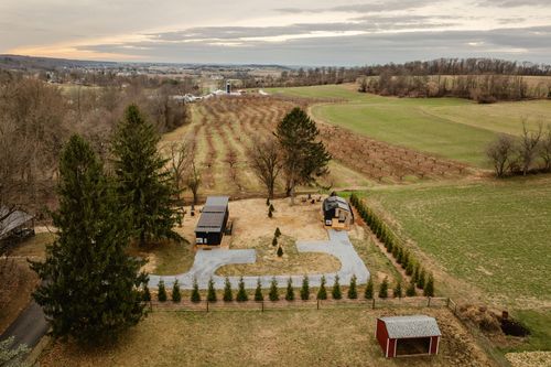 Aerial view of two black cabins with a curved gravel driveway surrounded by farmland at dusk