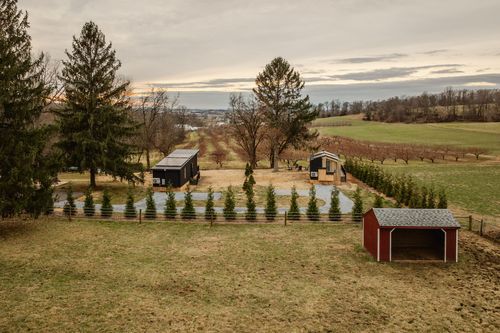 Aerial view of black cabins beside a red shed and evergreen rows framed by open farmland