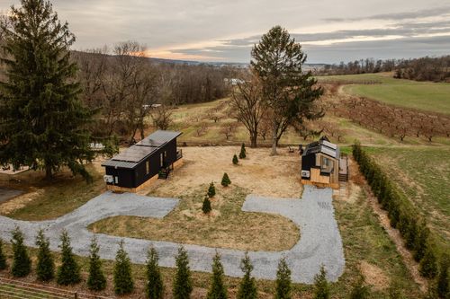 Aerial dusk view of black cabins on a curved driveway surrounded by orchard rows