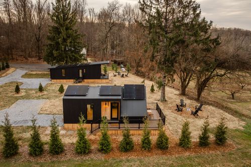 Aerial view of two black cabins with rooftop solar panels, lawn chairs and autumn woods