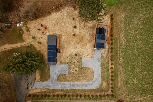 Aerial top-down view of two cabins with solar panels, gravel driveway and orchard rows